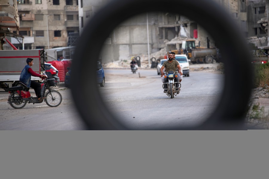 Due uomini in moto, ripresi attraverso uno pneumatico, passano davanti a edifici danneggiati durante la guerra civile a Homs, in Siria, giovedì 1 ottobre 2026. (Foto AP/Ghaith Alsayed) (APN)