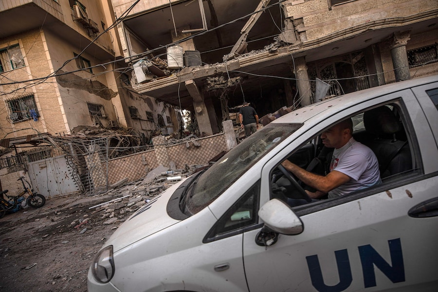 Un’auto delle Nazioni Unite transita nei pressi delle macerie di un condominio residenziale in seguito a un attacco aereo israeliano nella zona occidentale della città di Gaza (EPA)