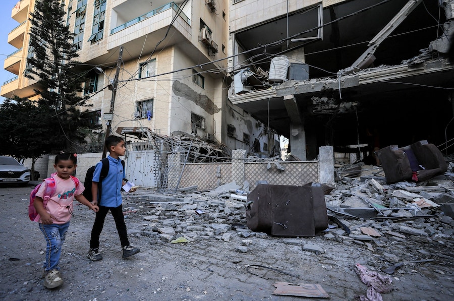 Bambini palestinesi passano davanti al luogo in cui si è verificato un attacco israeliano contro un condominio nella città di Gaza (REUTERS)