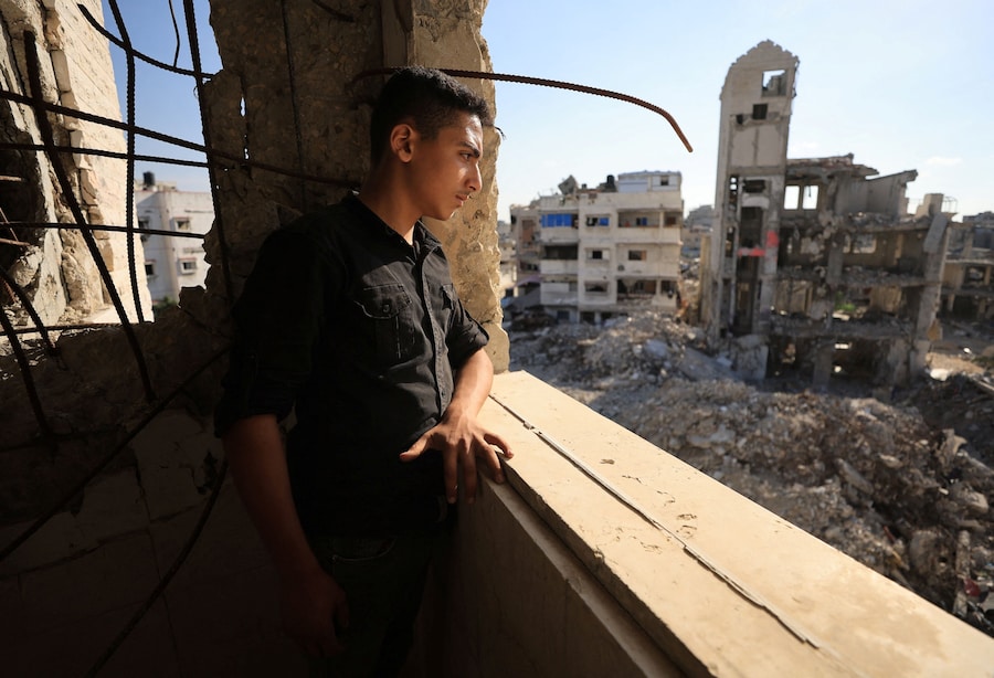 Un giovane palestinese guarda dalla finestra le macerie di alcuni edifici residenziali distrutti durante la guerra, nella città di Gaza (REUTERS)