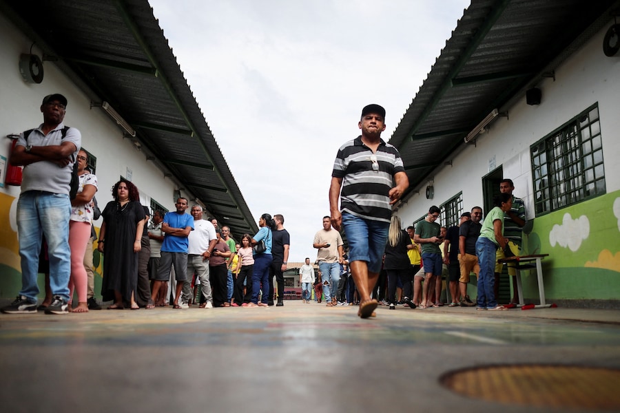 Un uomo cammina mentre la gente aspetta in fila per votare durante le elezioni generali brasiliane in un seggio elettorale situato in una scuola a Vila Estrutural, alla periferia di Brasilia, in Brasile. (REUTERS)