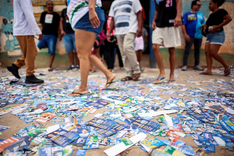 Le persone camminano sui volantini elettorali sparsi per terra mentre si radunano per votare in occasione delle elezioni generali brasiliane presso un seggio elettorale situato in una scuola a Sol Nascente, a Brasilia, in Brasile. (REUTERS)