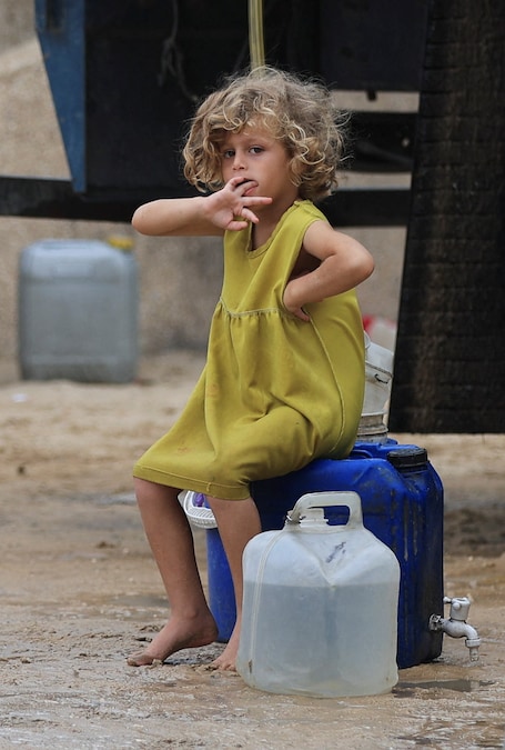 Una bambina palestinese è seduta su un contenitore d'acqua presso un punto di distribuzione idrica mobile, nella città di Gaza (REUTERS)