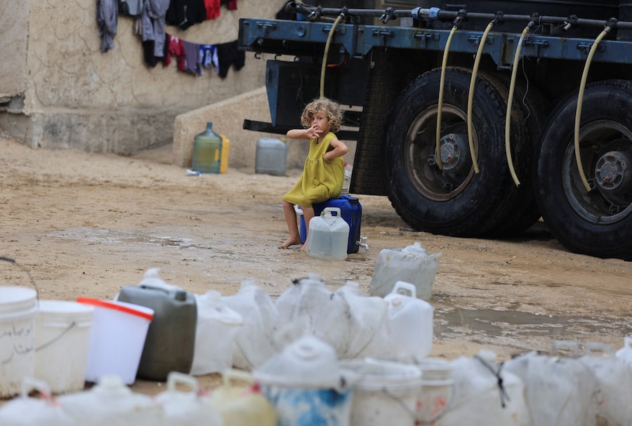 Una bambina palestinese è seduta su un contenitore d'acqua presso un punto di distribuzione idrica mobile, nella città di Gaza (REUTERS)