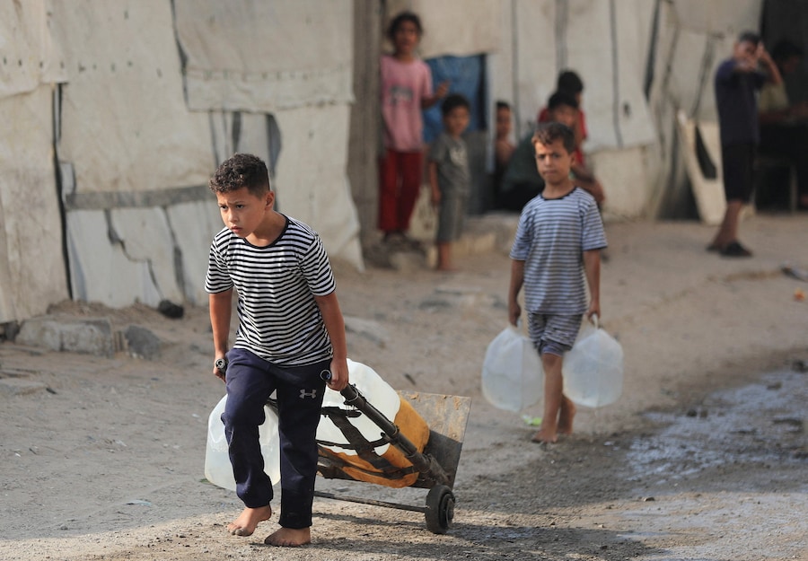 Bambini palestinesi trasportano l'acqua mentre tornano alle loro tende dopo averla prelevata in un campo tendato nella città di Gaza (REUTERS)