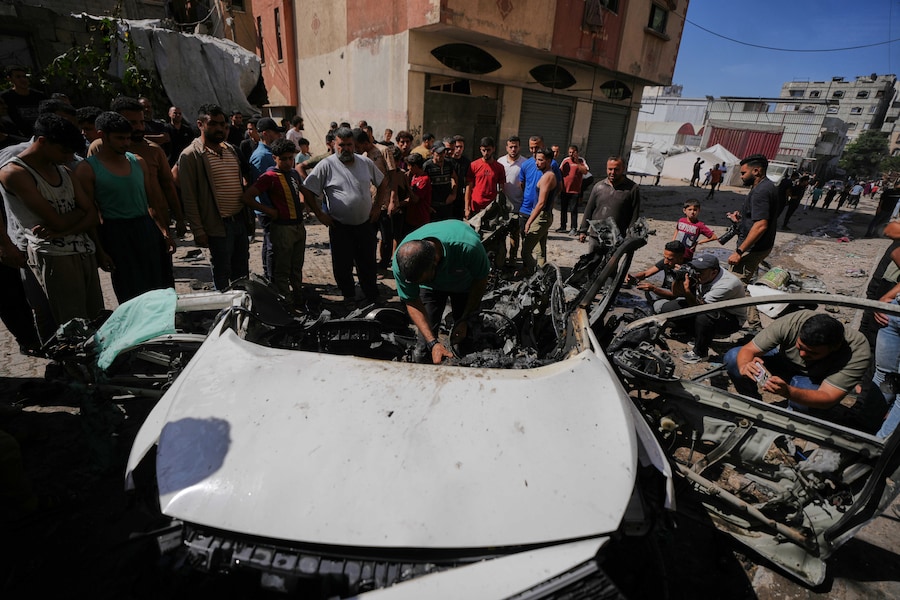 I palestinesi ispezionano i rottami di un’auto colpita da un attacco israeliano nella città di Gaza (APN)