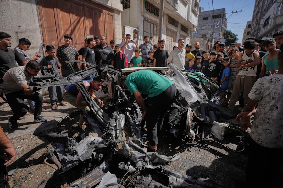 I palestinesi ispezionano i rottami di un’auto colpita da un attacco israeliano nella città di Gaza (APN)