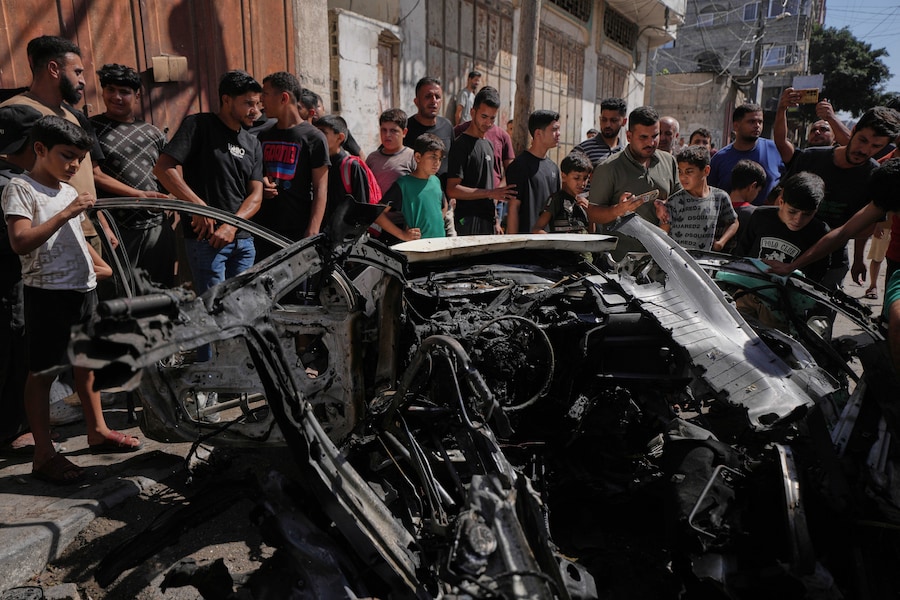 I palestinesi ispezionano i rottami di un’auto colpita da un attacco israeliano nella città di Gaza (APN)
