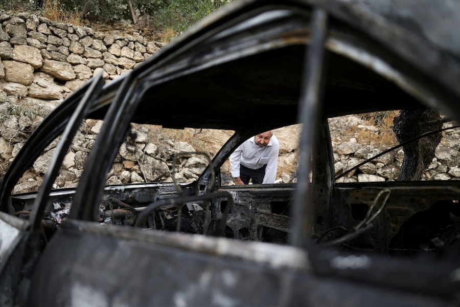 Un palestinese ispeziona un'auto danneggiata, che secondo i palestinesi sarebbe stata incendiata dai coloni israeliani, a Mukhmas, nei pressi di Ramallah, nella Cisgiordania occupata da Israele (REUTERS)