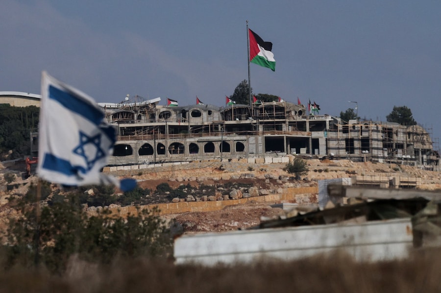 Una bandiera israeliana sventola mentre in lontananza sventolano bandiere palestinesi nei pressi di Ramallah, nella Cisgiordania occupata da Israele (REUTERS)