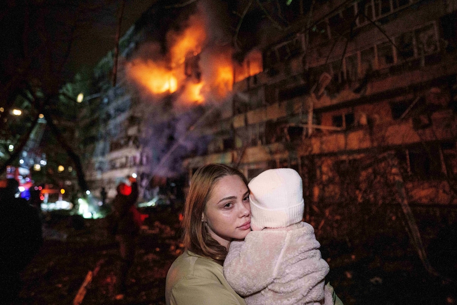 Victoria Deineko tiene in braccio sua figlia Mia mentre si trova davanti a un edificio residenziale a più piani danneggiato da un attacco missilistico russo a Kiev (APN)