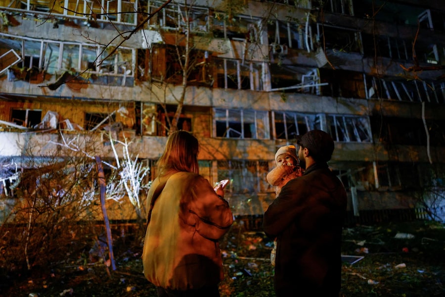 Un uomo porta in braccio un bambino sul luogo di un condominio danneggiato da un attacco missilistico russo a Kiev, Ucraina (REUTERS)
