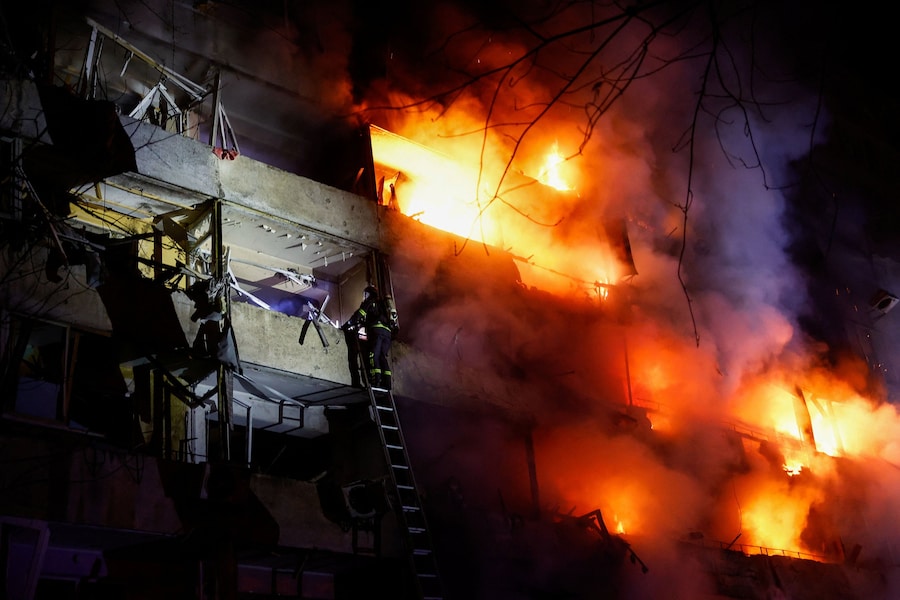 Un pompiere sale su una scala mentre fumo e fiamme si levano da un condominio danneggiato da un attacco missilistico russo a Kiev (REUTERS)