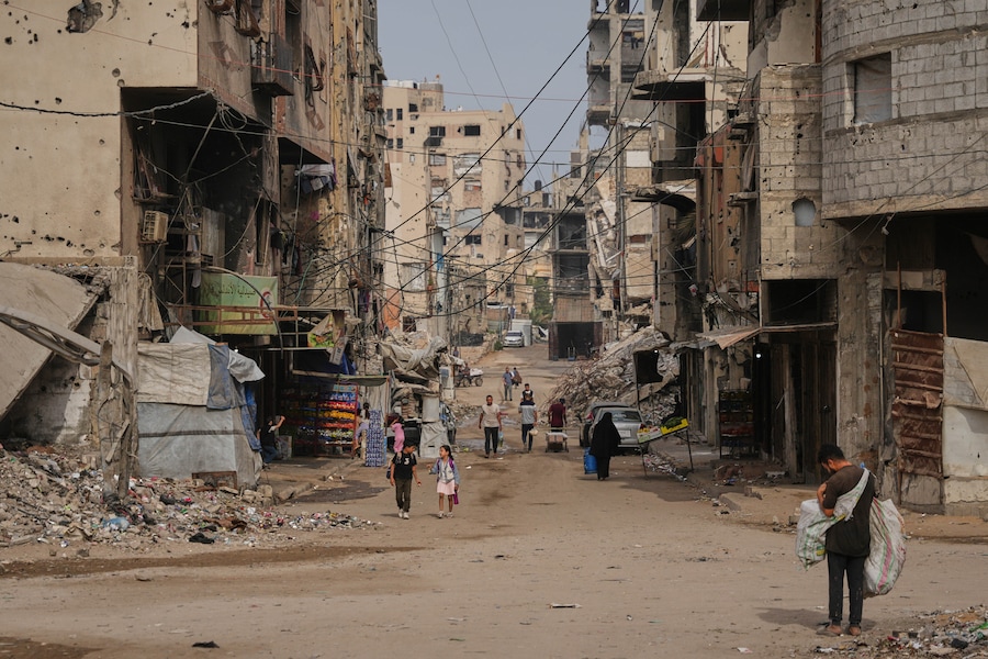 Alcuni palestinesi passano davanti a edifici danneggiati durante la guerra tra Israele e Hamas, nella città di Gaza. (Foto AP/Abdel Kareem Hana) (APN)