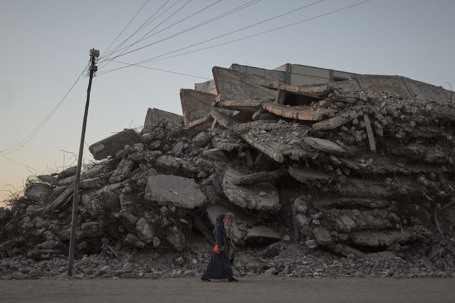 Due donne palestinesi camminano lungo una strada fiancheggiata da edifici distrutti durante la guerra tra Israele e Hamas nella città di Gaza. (Foto AP/Jehad Alshrafi) (APN)