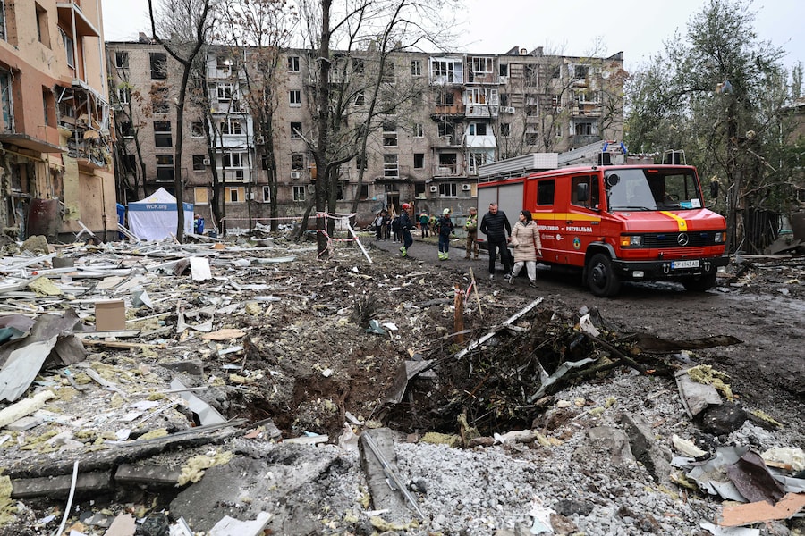 Sabato 17 ottobre 2026, alcune persone passano davanti a un cratere sorto davanti a un edificio residenziale danneggiato da un attacco aereo russo a Zaporizhzhia. (APN)