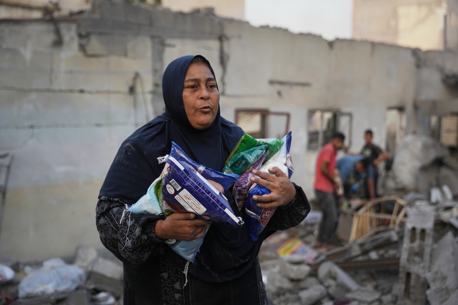 Una donna palestinese trasporta sacchi di zucchero, tutto ciò che è riuscita a recuperare dalla sua casa dopo che questa è stata distrutta durante un attacco israeliano, a Nuseirat, nella Striscia di Gaza centrale (APN)