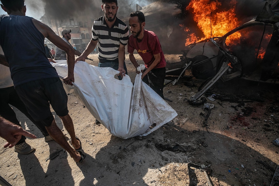 Alcuni palestinesi recuperano un corpo da un veicolo distrutto in un attacco aereo israeliano a sud di Gaza City (EPA)