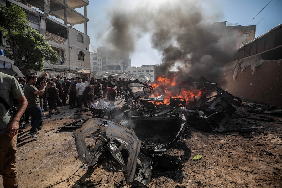 Alcuni palestinesi ispezionano un veicolo in fiamme distrutto da un attacco aereo israeliano a sud della città di Gaza (EPA)