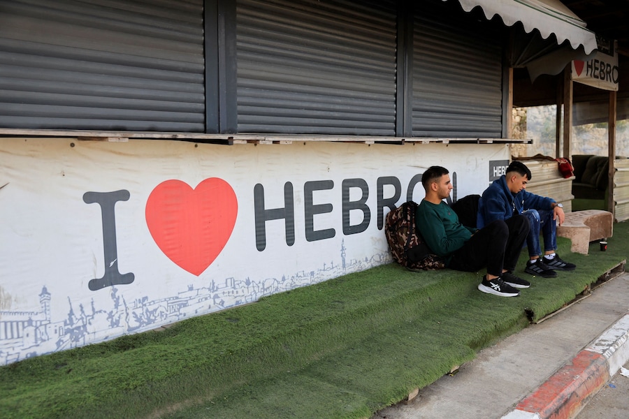 Palestinesi seduti vicino all'ingresso chiuso di Hebron, nella Cisgiordania occupata da Israele, il 24 ottobre 2026. (REUTERS)