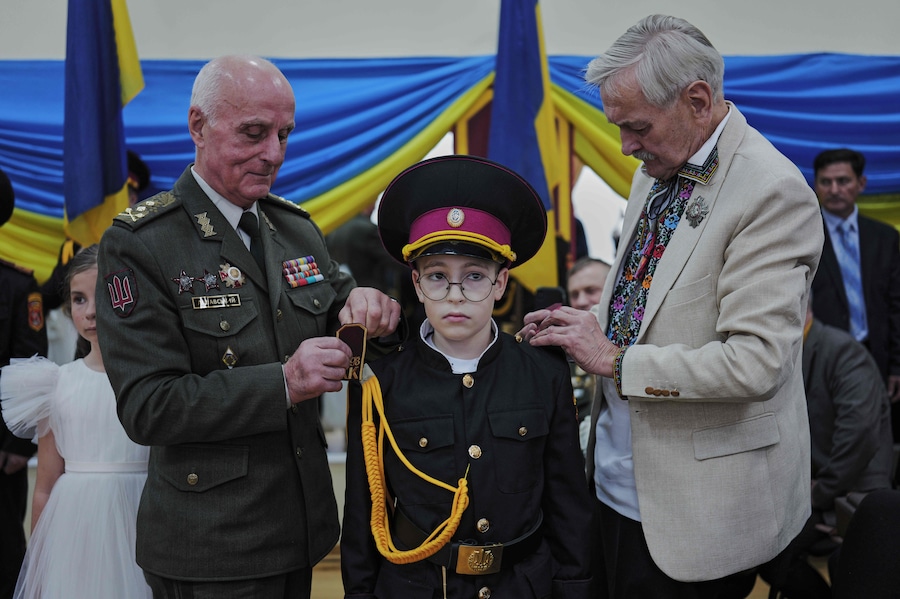 Il generale dell'esercito ucraino Volodymyr Lishavsky e l'attore Volodymyr Talashko applicano le spalline a un giovane cadetto durante la cerimonia di iniziazione in un liceo militare a Kiev, venerdì 23 ottobre 2026. (APN)