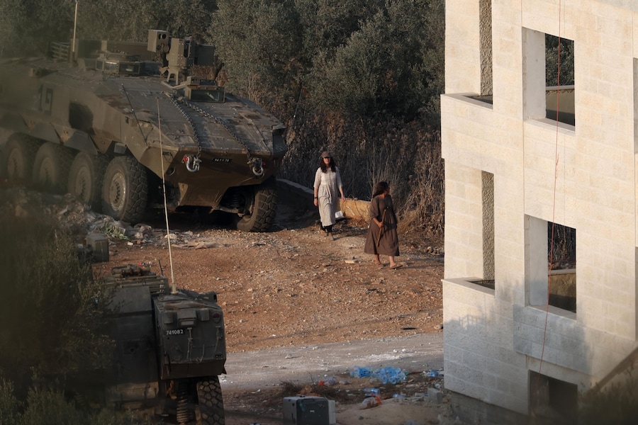 Coloni israeliani passano accanto a un veicolo blindato dell’esercito israeliano, di stanza nei pressi di un edificio occupato, durante la raccolta annuale delle olive nella città palestinese di Turmus Ayya, in Cisgiordania, il 24 ottobre 2026. (EPA)