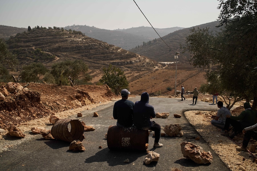Alcuni uomini palestinesi sono seduti lungo una strada, bloccata nel tentativo di impedire ai coloni israeliani di entrare nella zona, nelle vicinanze della città di Sinjil, in Cisgiordania, sabato 24 ottobre 2026. (APN)