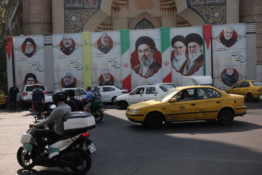 Alcune persone guidano accanto a uno striscione con l’immagine della Guida Suprema dell’Iran Mojtaba Khamenei, in una strada di Teheran. (Majid Asgaripour/WANA (West Asia News Agency) via REUTERS)