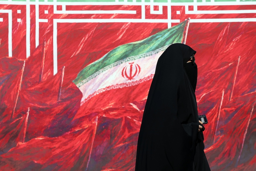 Una donna iraniana passa davanti a un cartellone pubblicitario raffigurante la bandiera nazionale iraniana, in una strada di Teheran. (EPA/Abedin Taherkenareh)