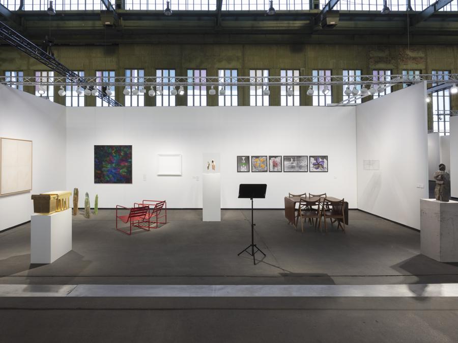 Lo stand di Esther Schipper (Berlino) alla fiera Art Berlin 2019, una presentazione collettiva con un richiamo al tema del ritratto attraverso le opere di diversi artisti tra cui AA Bronson con due bamboline voodoo rappresentanti se stesso e suo marito, Simon Fujiwara con un ritratto della Germania attraverso un dispositivo per riciclare la spazzatura ricoperto d'oro e uno di Angela Merkel attraverso un dettaglio della sua pelle dipinto con il makeup che usa da sempre, Jean-Pascal Flavien con due sedie intrecciate ispirate ad un ritratto di una coppia faraonica, Ugo Rondinone con una delle sue sculture in pietra del corpo umano (prezzi non dichiarati, Photo credit Andrea Rossetti, Courtesy Esther Schipper)