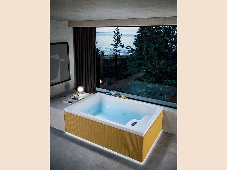 Glass 1989, Mawi Spa. Mini piscina per indoor e outdoor. Qui, nella versione in appoggio, è proposta con pannellature in LYCRA® XTRA LIFE™, un tessuto tecnico utilizzato anche nello swimwear. Il tessuto di cui sono rivestiti i pannelli, disponibile in quattro colori, è particolarmente adatto per l'uso spa, perché è idrorepellente e si asciuga rapidamente ed è caratterizzato da alta resistenza all'abrasione e ai raggi UV, ultra resistenza agli agenti chimici, elasticità e morbidezza al tatto, oltre ad essere anti macchia. La gamma Mawi Spa è dotata di un sistema di ricircolo di ultima generazione estremamente silenzioso, che rende ideale per l'uso indoor. Lo Skimmer con filtro a cartuccia, coniuga prestazioni ottimali e dimensioni compatte, massimizzando lo spazio interno delle vasche. La rubinetteria termostatica a scomparsa consente un rapido riempimento della Spa alla temperatura preimpostata. Il sistema di rabbocco automatico mantiene costante il livello dell'acqua per un benessere totale, l'ozonizzatore automatico aumenta l'efficacia del sistema filtrante, neutralizza la proliferazione batterica, e garantisce massima igiene. La versione in appoggio con pannellatura è arricchita di una luce perimetrale emozionale