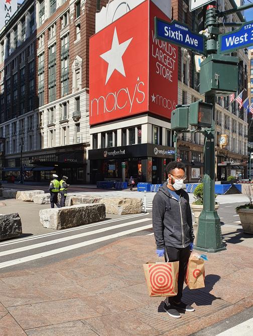 Un ragazzo con le buste della spesa e la mascherina davanti ai magazzini Macy's.