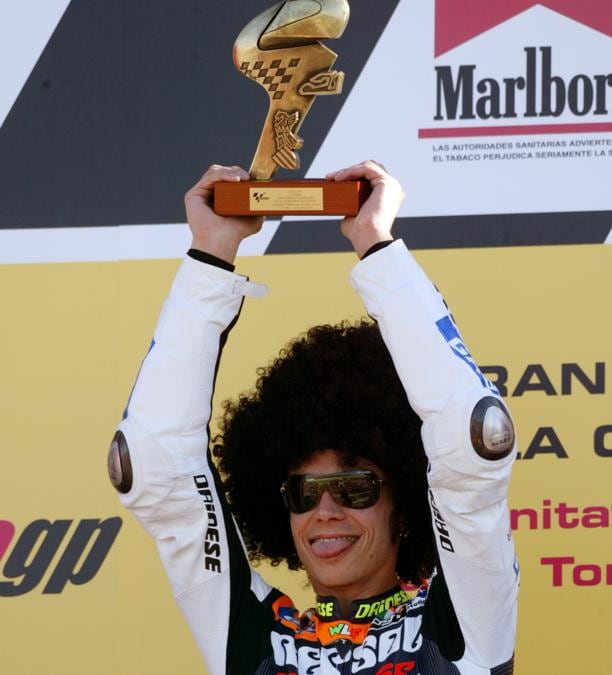 Italian MotoGP world champion Valentino Rossi, wearing a comical wig, holds the trophy on the podium after winning the Valencia Motorcycle Grand Prix at the Ricardo Tormo circuit, southeast of Spain November 2, 2003. Rossi won the race, Spaniard Sete Gibernau finished second and Italian Loris Capirossi third. REUTERS/Gustau Nacarino GN/CRB