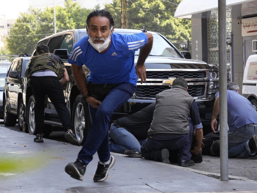 Un uomo corre per mettersi al riparo mentre i sostenitori di un gruppo sciita alleato con Hezbollah aiutano gli uomini feriti durante gli scontri armati scoppiati durante una protesta nel sobborgo meridionale di Beirut, Dahiyeh, in Libano, giovedì 14 ottobre 2021. Non è stato immediatamente chiaro cosa ha innescato gli spari, ma la tensione era alta lungo un’ex prima linea di guerra civile tra aree musulmane sciite e cristiane. (AP Photo/Hassan Ammar)