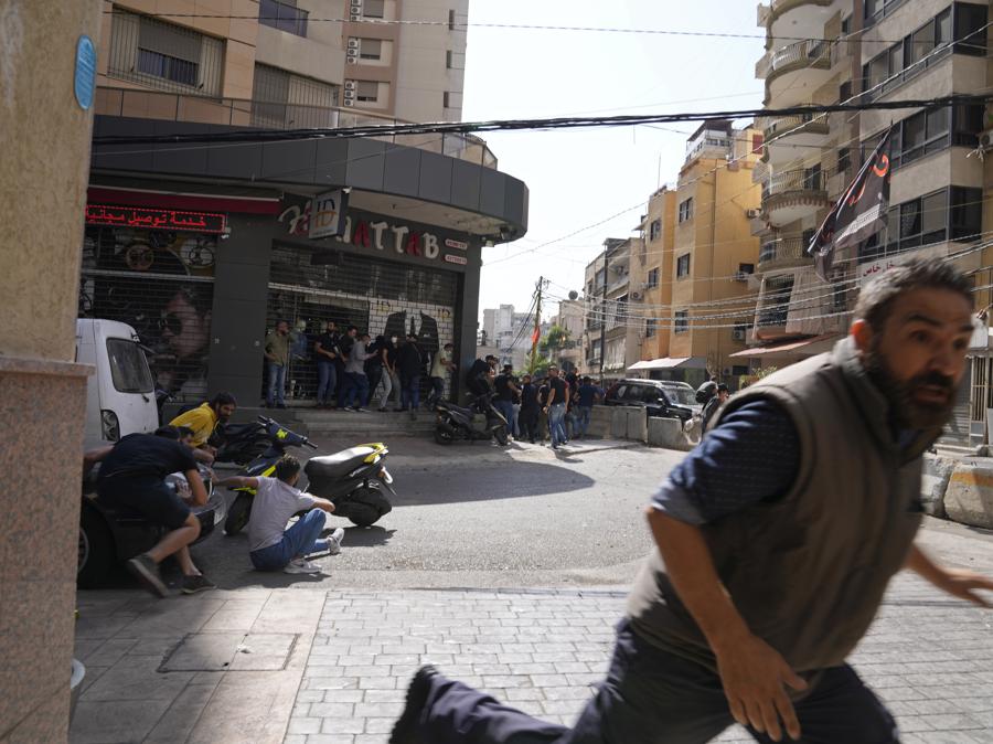 Un uomo corre per mettersi al riparo come sostenitori di un gruppo sciita alleato con armi da fuoco di Hezbollah durante gli scontri armati scoppiati durante una protesta nel sobborgo meridionale di Beirut di Dahiyeh, in Libano, giovedì 14 ottobre 2021. Non è stato immediatamente chiaro cosa abbia innescato gli spari, ma le tensioni erano alte lungo un’ex prima linea di guerra civile tra aree musulmane sciite e cristiane. (AP Photo/Hassan Ammar)