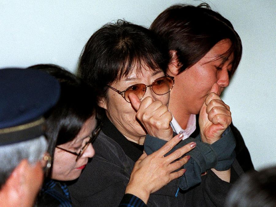 Fusako Shigenobu (centro), fondatrice dell’Armata Rossa giapponese, è scortata da agenti di polizia nella stazione di Tokyo l’8 novembre 2000 dopo essere stata arrestata a Osaka. (Photo by JIJI PRESS / AFP) / Japan OUT
