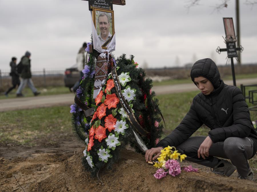 Yura Nechyporenko, 15 anni, depone un cioccolato sulla tomba di suo padre Ruslan Nechyporenko nel cimitero di Bucha, alla periferia di Kiev, in Ucraina. (AP Photo/Petros Giannakouris)