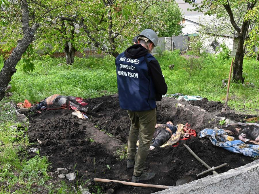 Un investigatore sta accanto ai corpi riesumati da una tomba nel cortile di una casa nel villaggio di Stepanky, vicino a Kharkiv. (Photo by SERGEY BOBOK / AFP)
