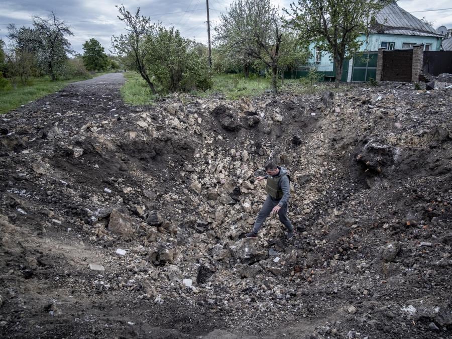 Un uomo esamina il cratere dell’esplosione nel centro del villaggio di Slatino nella regione di Kharkiv. EPA/MARIA SENOVILLA