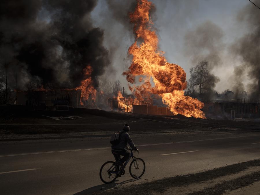 Un uomo guida la sua bicicletta tra le fiamme e il fumo che si alza da un incendio in seguito a un attacco russo a Kharkiv. (AP Photo/Felipe Dana)