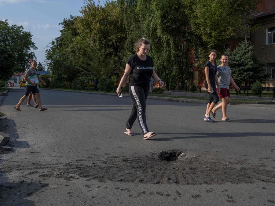 La gente cammina accanto a un cratere lasciato da un bombardamento delle forze russe nella città ucraina di Marhanets. (Photo by BULENT KILIC / AFP)
