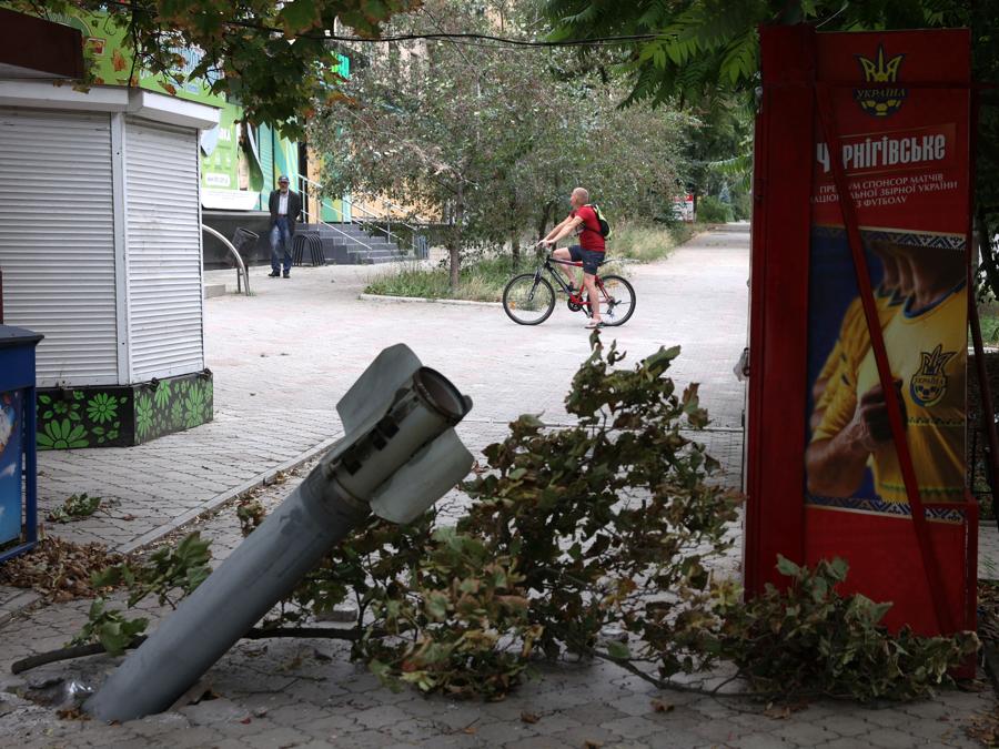 Un residente locale passa in bicicletta davanti a un frammento di un razzo conficcato nel terreno a seguito di un attacco missilistico nella città di Bakhmut. (Photo by Anatolii Stepanov / AFP)