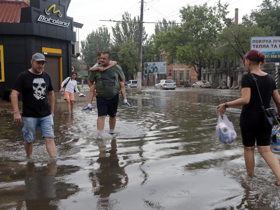 La gente cammina attraverso una strada allagata a seguito di forti piogge nel porto ucraino di Odessa, sul Mar Nero. (Photo by OLEKSANDR GIMANOV / AFP)