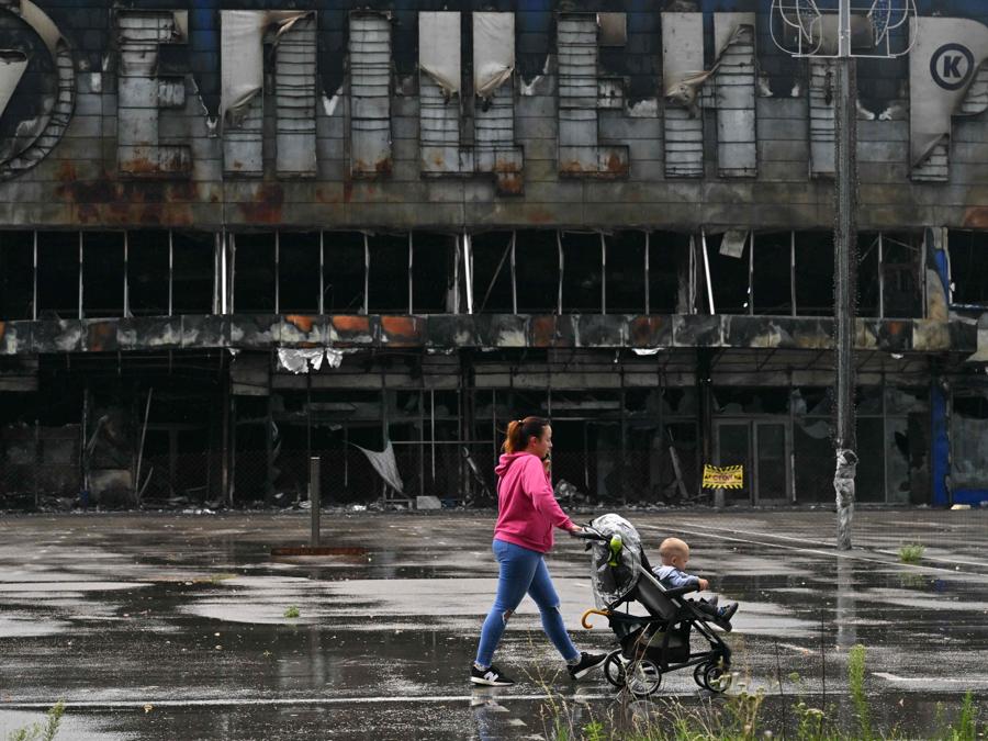 Una donna cammina con un bambino davanti a un centro commerciale distrutto a Bucha, nella regione di Kiev. (Photo by Sergei SUPINSKY / AFP)