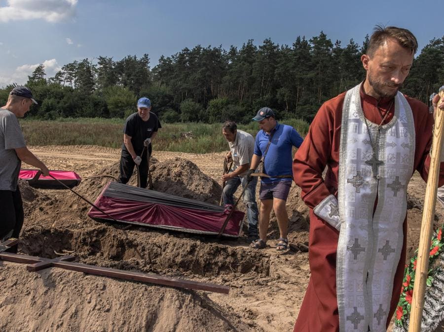 Operai calano una bara nella tomba contenente il corpo di una persona non identificata uccisa nel distretto di Bucha. EPA/ROMAN PILIPEY