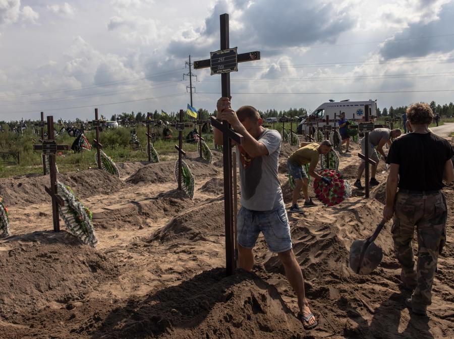Un lavoratore erige una croce sulla tomba di una persona non identificata uccisa nel distretto di Bucha. EPA/ROMAN PILIPEY