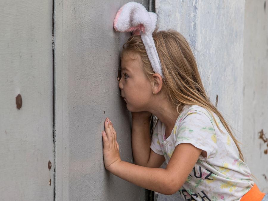 Una bimba guarda attraverso un buco di  una recinzione dopo un recente attacco militare russo. (Reuters/Oleksandr Ratushniak)