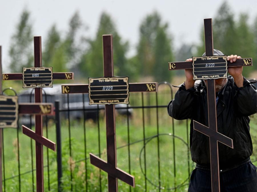 Un addetto municipale mette croci con numeri sulle tombe di dodici civili non identificati, sepolti in un cimitero di Bucha. (Photo by Sergei Supinsky / Afp)