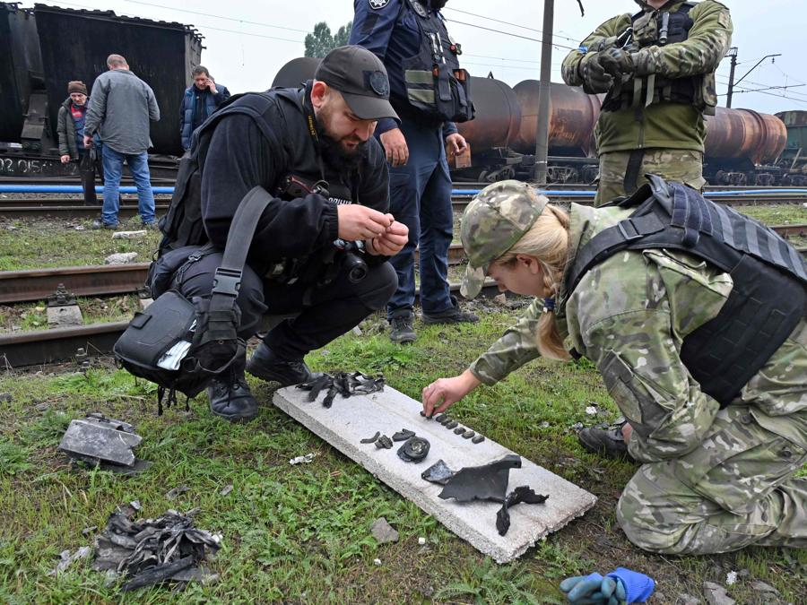 Un esperto forense di esplosivi e un esperto di polizia raccolgono frammenti di missili dopo un attacco a una stazione ferroviaria merci a Kharkiv. (Photo by Sergey Bobok / AFP)