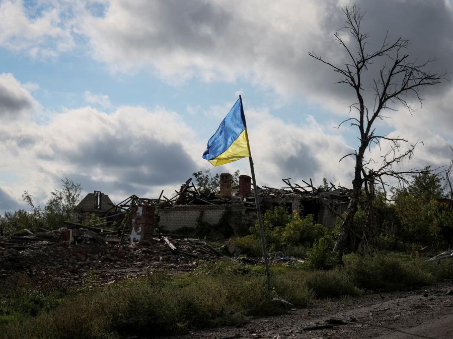 La bandiera nazionale ucraina sventola vicino ad alcuni edifici distrutti,  nel villaggio di Dolyna. (REUTERS/Gleb Garanich)
